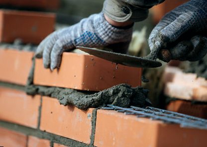 Mason's hands coursing new brick onto a fresh mortar bed